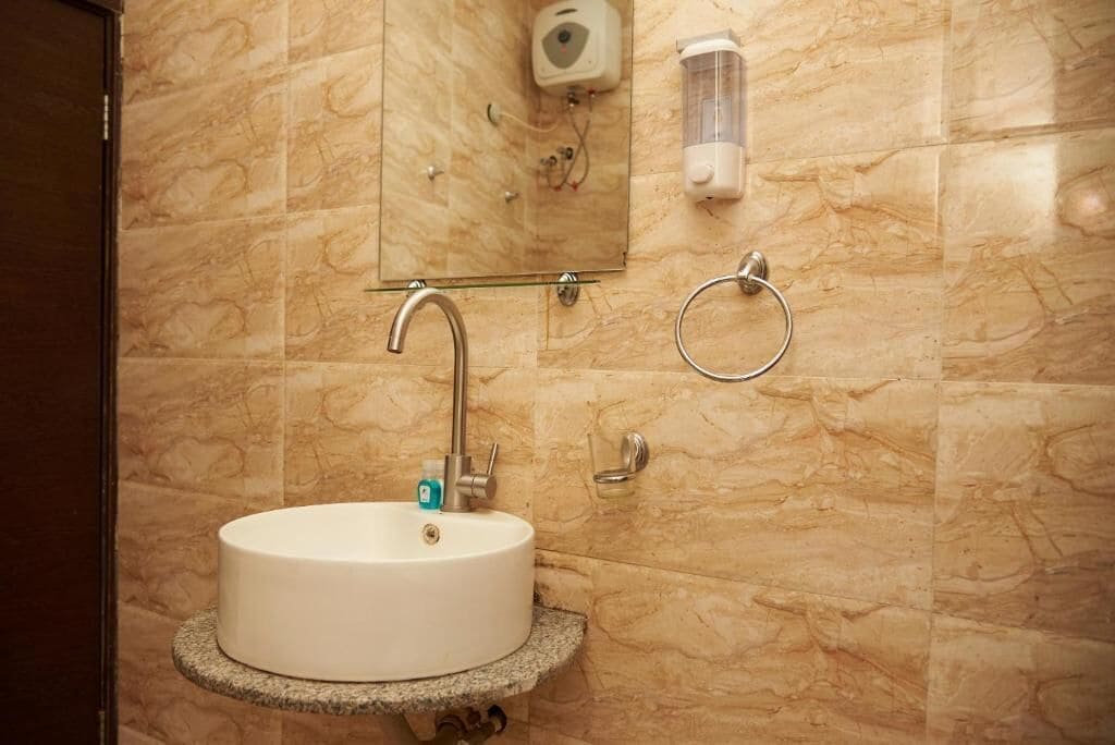 A bathroom with a marble wall, a sink with a faucet, a soap dispenser, and a towel ring.