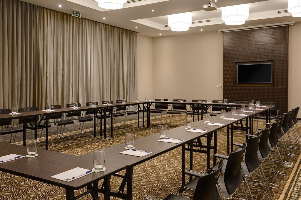 A conference room with long tables, chairs, and a large screen on the wall.