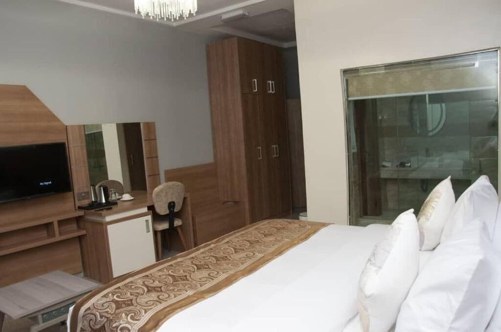 A hotel room with a bed, a desk, a television, a wardrobe, and a large window.