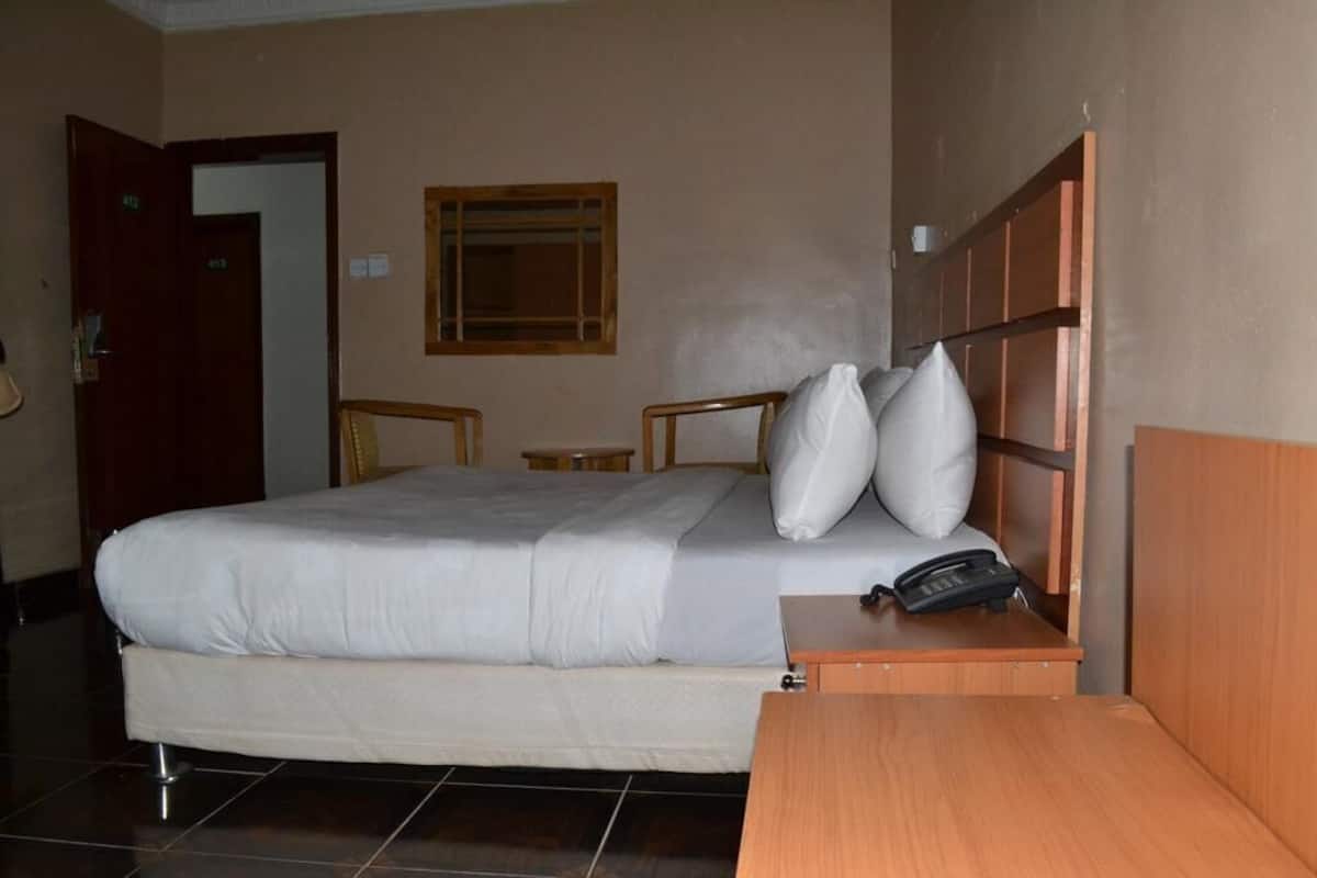 Una habitación de hotel con cama, mesita de noche y cabecero de madera.