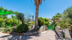 A paved pathway leading to a gated entrance, surrounded by lush greenery and a palm tree. - Finca Salrima Álora by Ruralidays (Málaga)