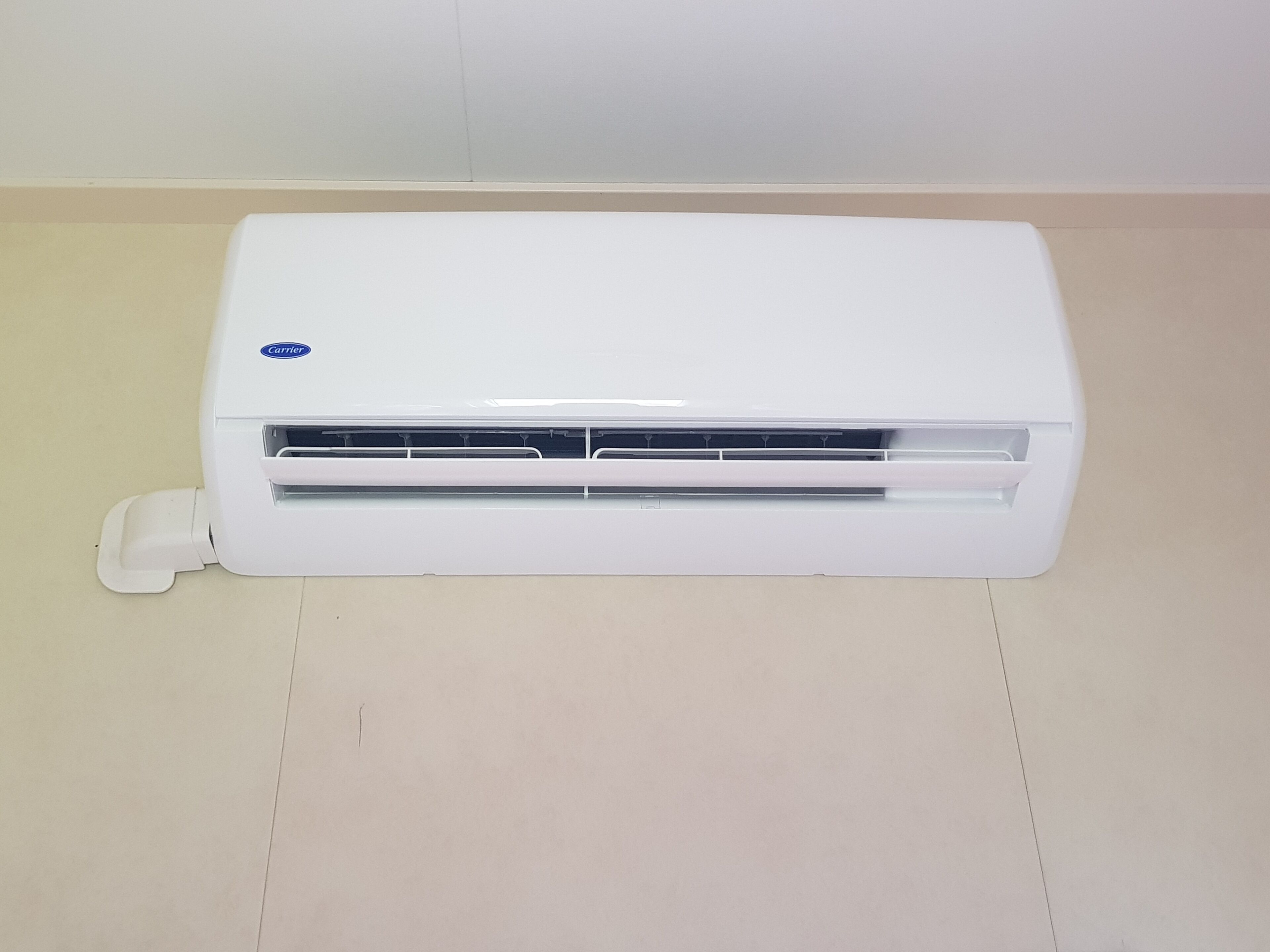 Een witte airconditioningunit met Carrier logo, geplaatst op een betegelde vloer.
