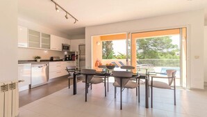 Een moderne keuken met witte kasten, een eethoek met een glazen tafel en stoelen, en een balkon met uitzicht op groen.