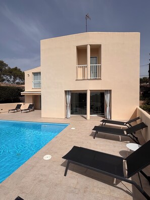 A modern building with a swimming pool, lounge chairs, and a covered patio area.