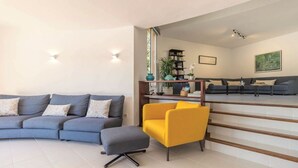 Een moderne woonkamer met een grijze bank, een gele fauteuil en een trap naar een andere kamer.