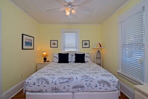Une chambre à coucher avec un lit, un ventilateur de plafond, une table de chevet avec une lampe et une fenêtre avec des stores.
