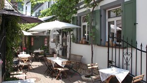 An outdoor café with tables and chairs, surrounded by buildings with green shutters and vines. - homie hotel oechsle & brix (Sommerhausen)