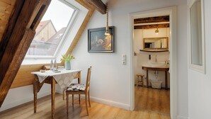 A dining area with a table and chairs, a window with a view, and a kitchen visible through an open door. - homie hotel oechsle & brix (Sommerhausen)