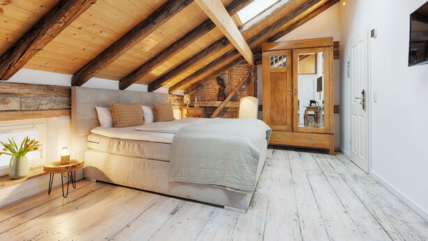 A bedroom with a sloped ceiling, a bed, a nightstand, a mirror, and a wardrobe. - homie hotel oechsle & brix (Sommerhausen)
