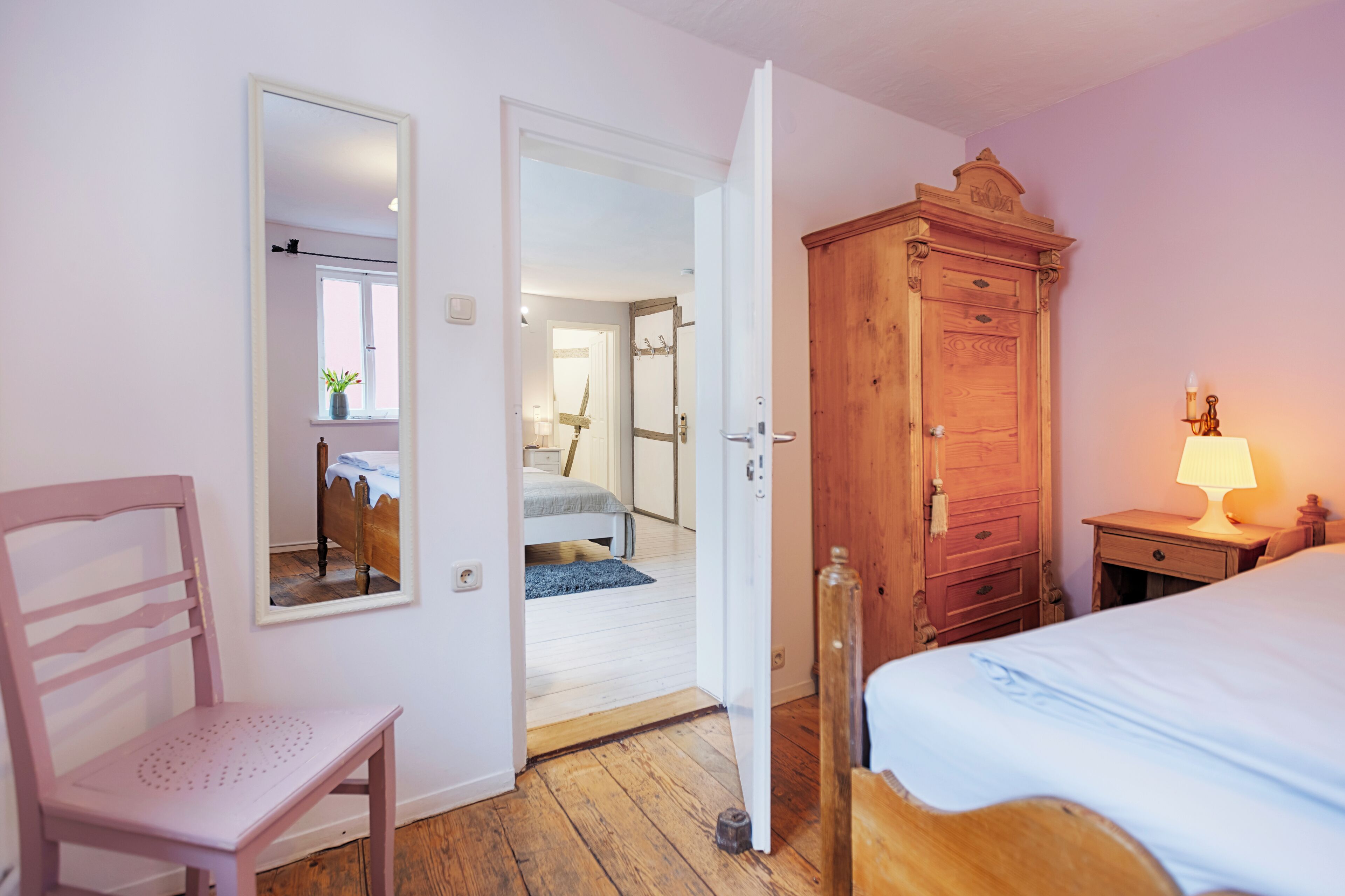 A bedroom with a wooden wardrobe, a bed, a chair, and a mirror.