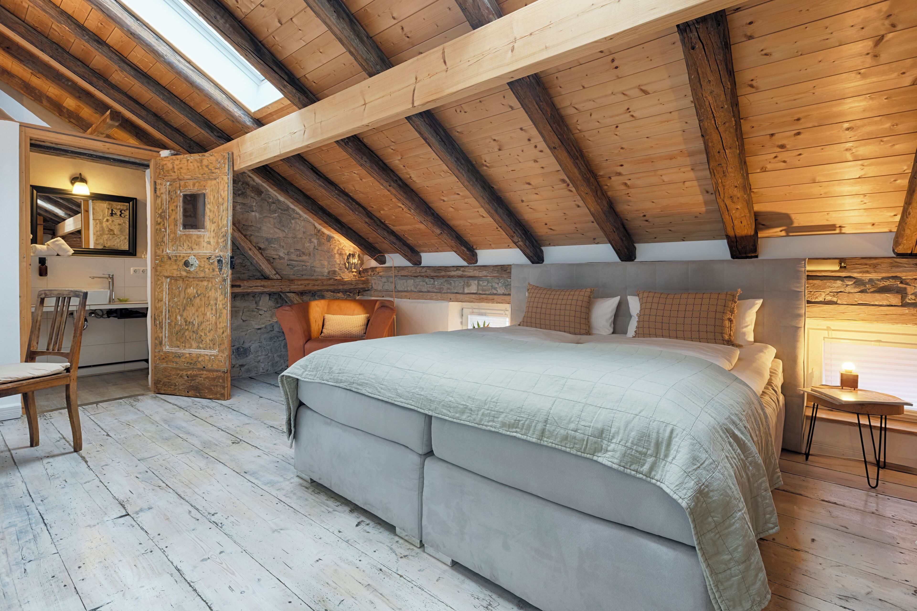 Une chambre à coucher avec un grand lit, des poutres en bois, un mur en pierre et une petite table avec une lampe.