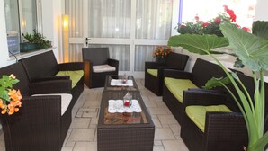 Un área de estar exterior amoblada con muebles de mimbre, una mesa de centro de vidrio y plantas en macetas.