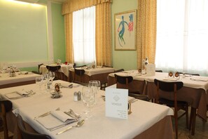 Un comedor de hotel con mesas preparadas para una comida, un cartel con el menú y un cuadro en la pared.