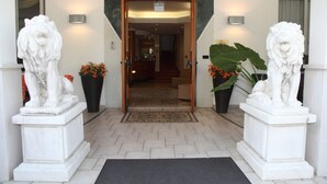 Una entrada de hotel con puertas dobles, dos estatuas de león y plantas en macetas.