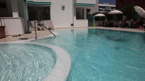 Una piscina con borde de azulejos, sillas de descanso y sombrillas.