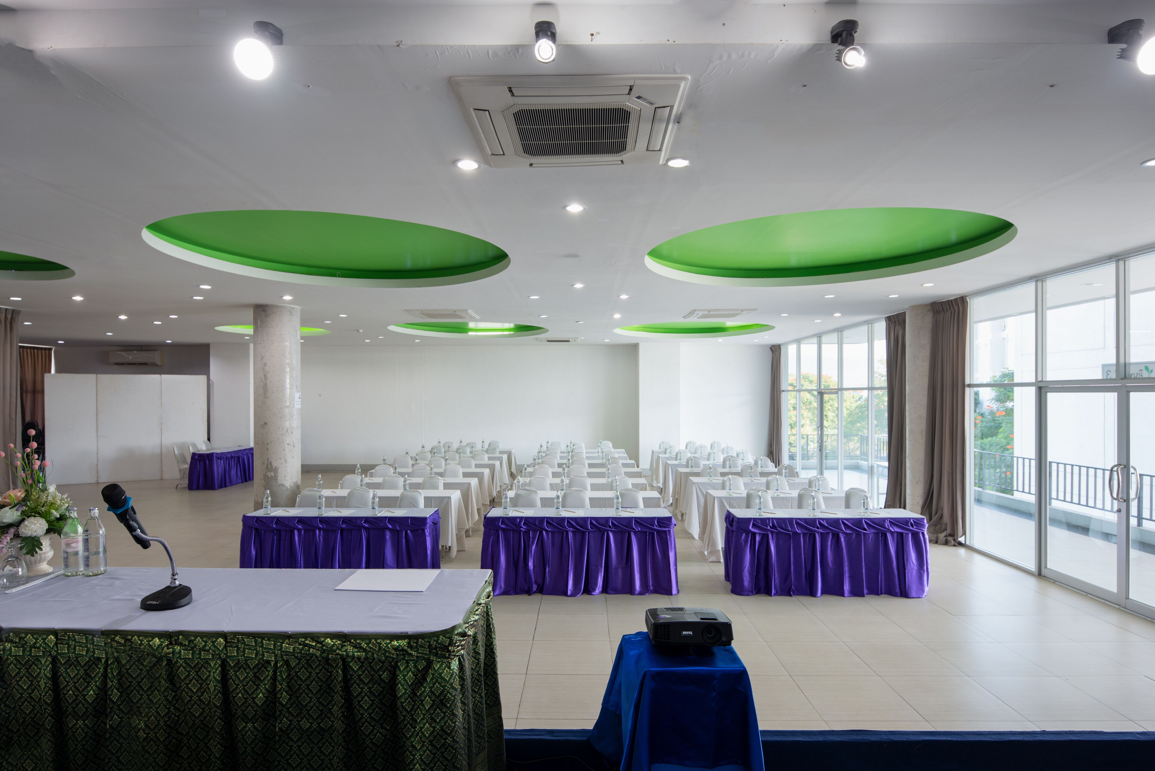 A conference room with rows of tables, purple tablecloths, and a microphone on a table.