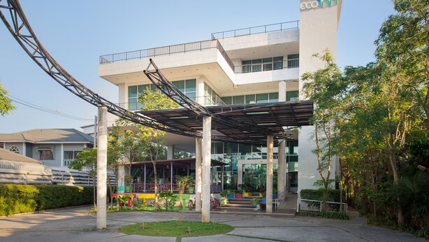 A modern building with a covered entrance, large windows, and a logo on the side. - Eco Inn Prime Mae Sot (Mae Sot)