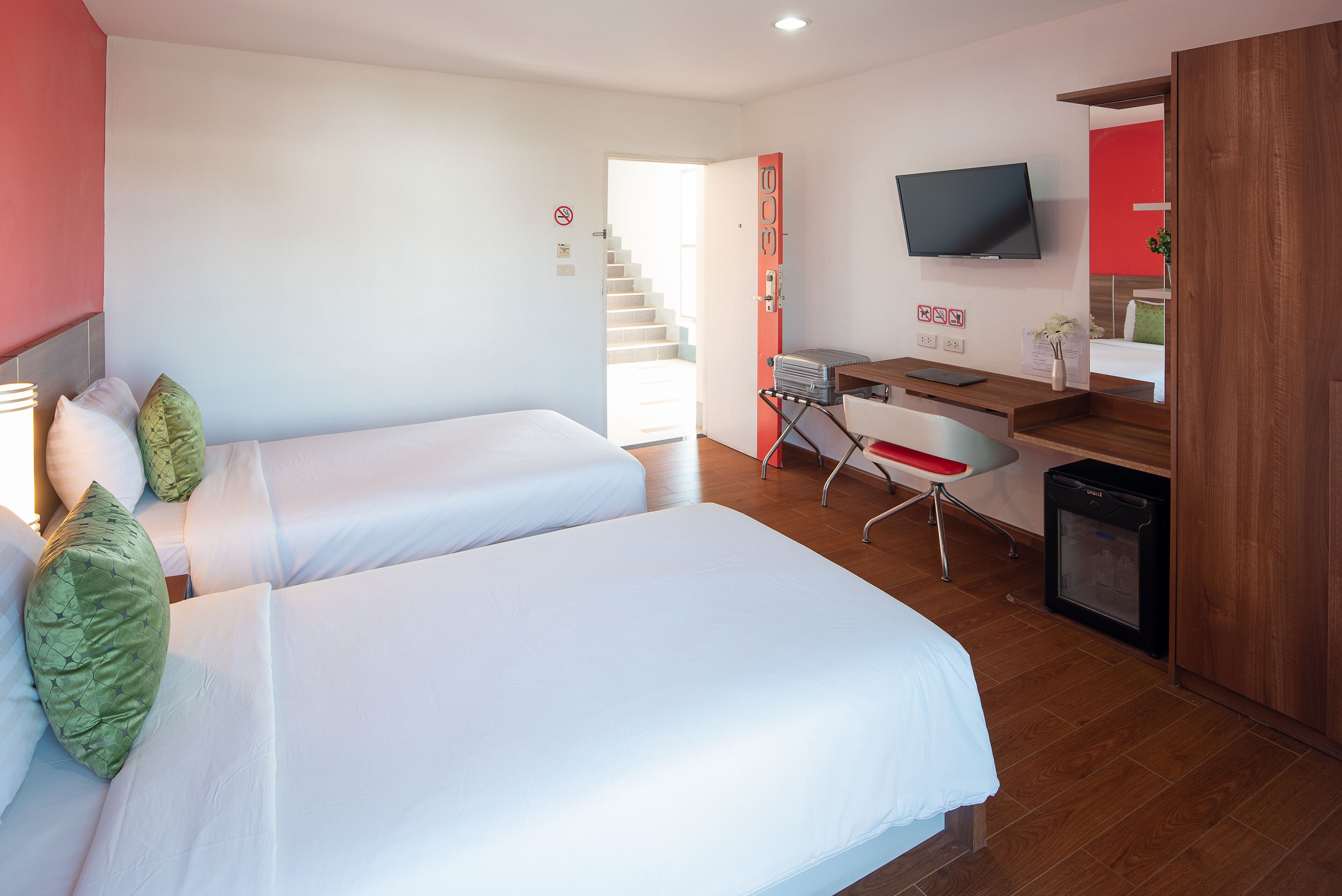 A hotel room with two beds, a desk with a chair, a television, and a small refrigerator.
