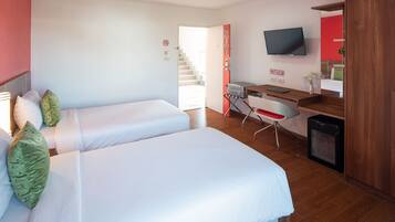 A hotel room with two beds, a desk with a chair, a television, and a small refrigerator.