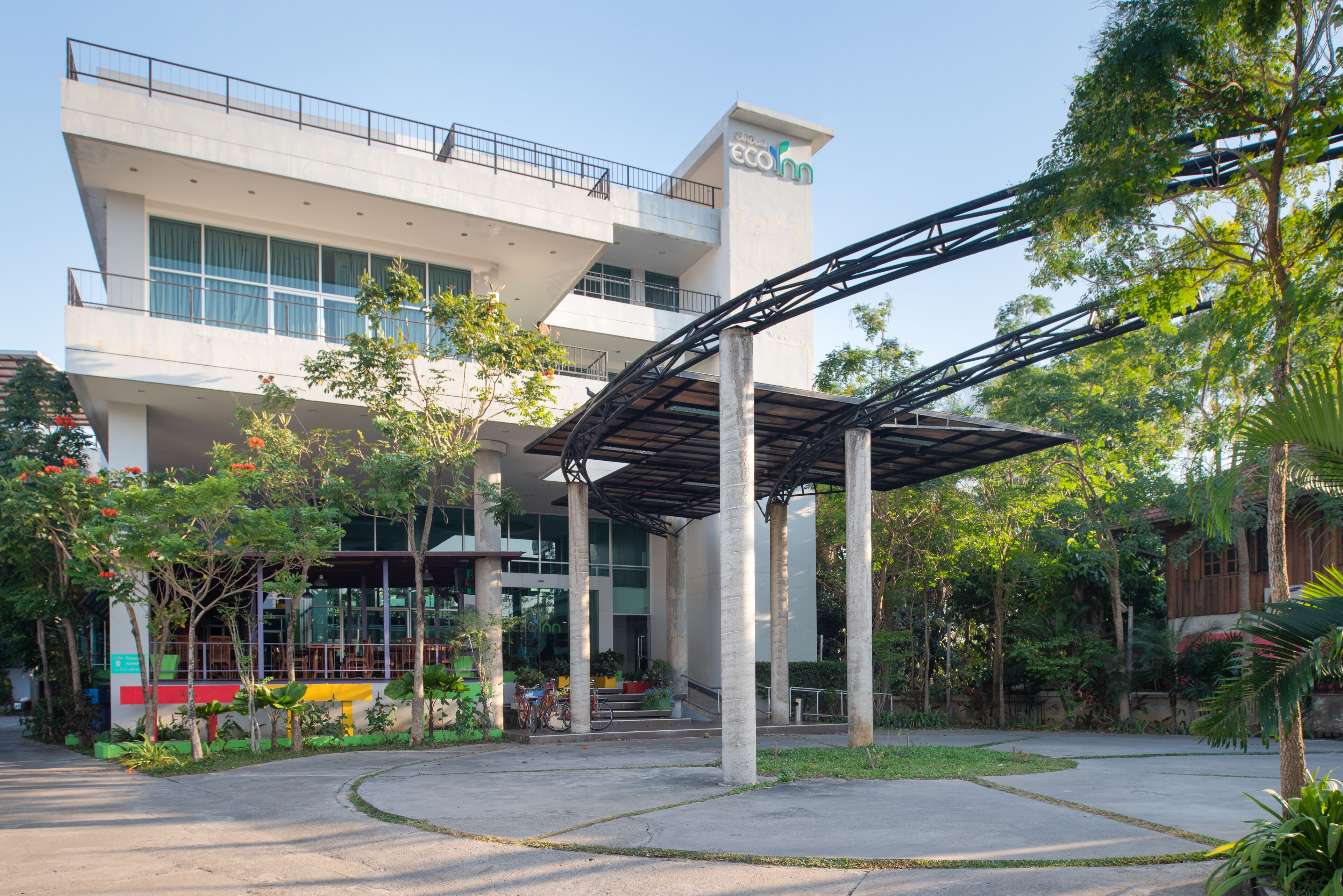 A modern building with a covered entrance and a garden area with trees and plants.