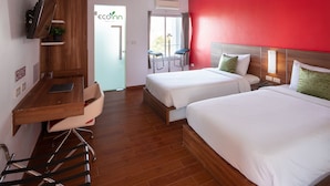 A hotel room with two beds, a desk with a laptop, a chair, and a red accent wall. - Eco Inn Prime Mae Sot (Mae Sot)