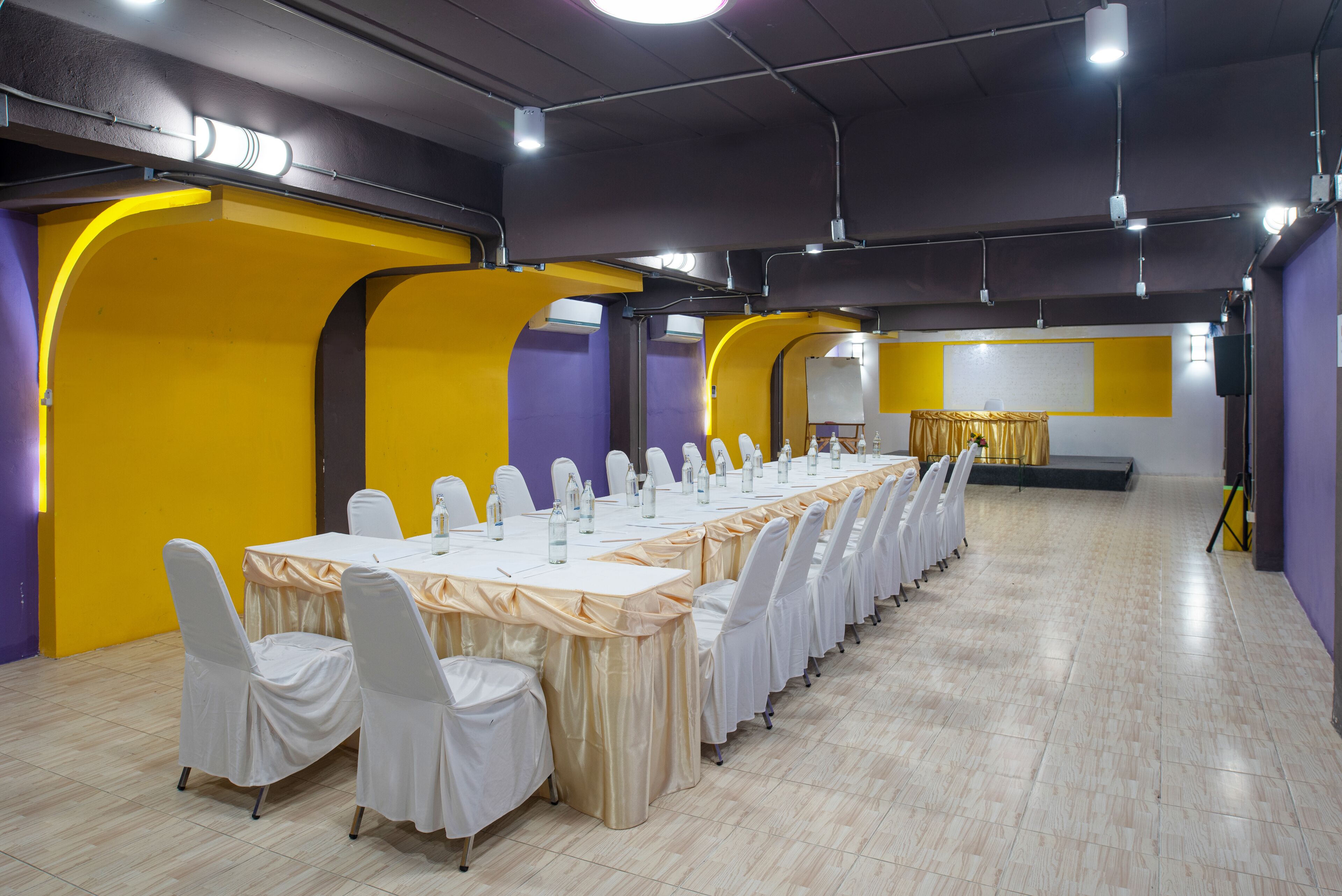 Una sala de conferencias con una larga mesa, sillas blancas y un escenario.