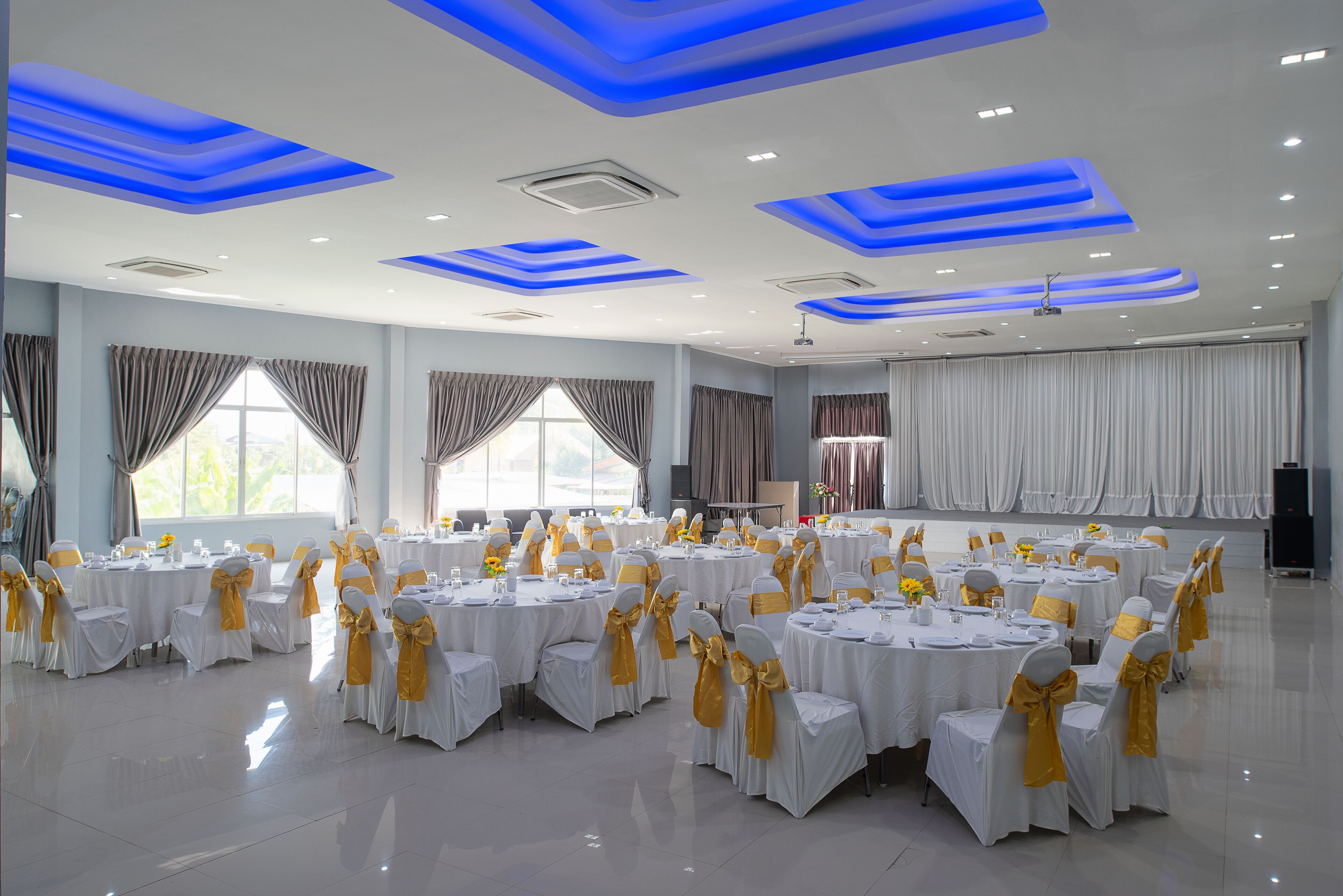 Un salón de banquetes con mesas redondas, manteles blancos y sillas adornadas con cintas amarillas.
