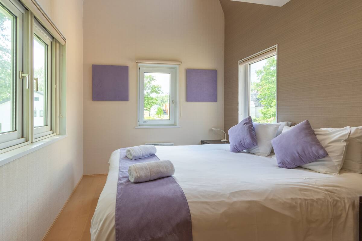 A bedroom with a large bed, two windows, and a view of trees.