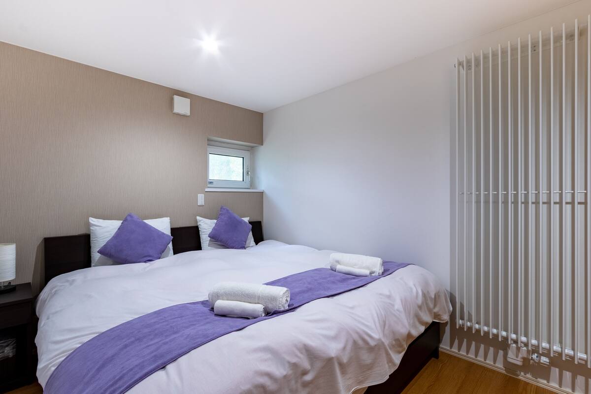 A hotel room with a large bed, two pillows, a window, and a radiator.
