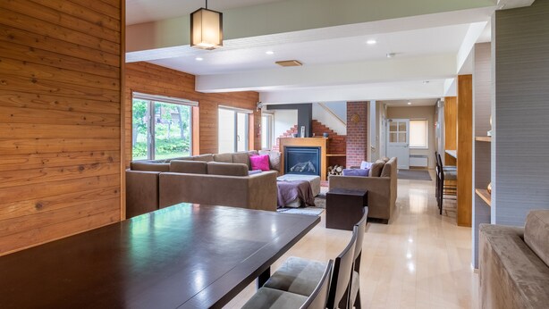 A modern living room with a wooden accent wall, a fireplace, and a dining area with a long table and chairs. - Cisco Moon (Kutchan)