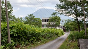 A narrow road leading to a modern building with a mountain in the background. - Cisco Moon (Kutchan)