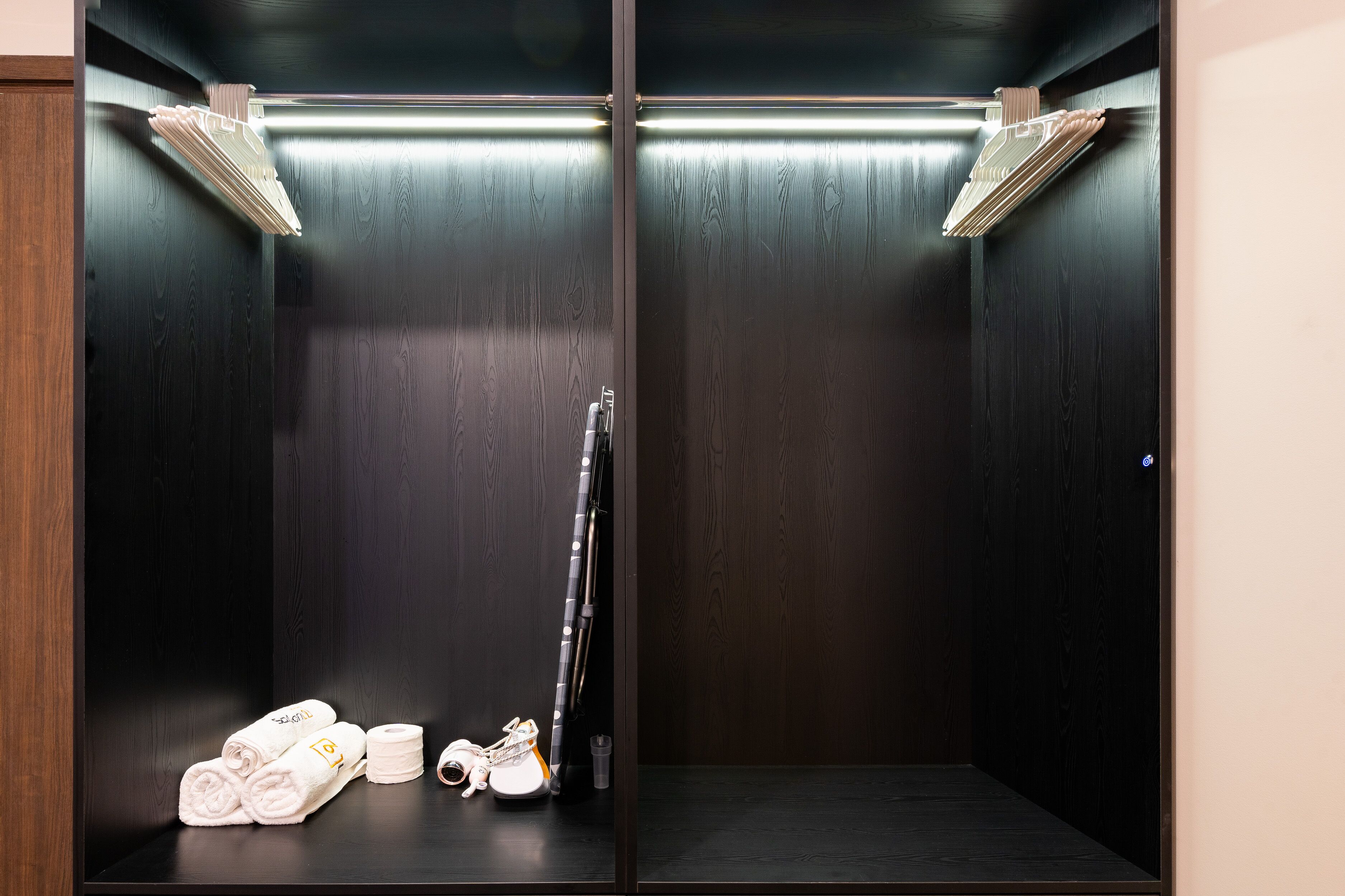 Egy sötét színű, fából készült lift, melynek a padlója sík, van benne egy törölközőtartó, és egy pár cipő.
