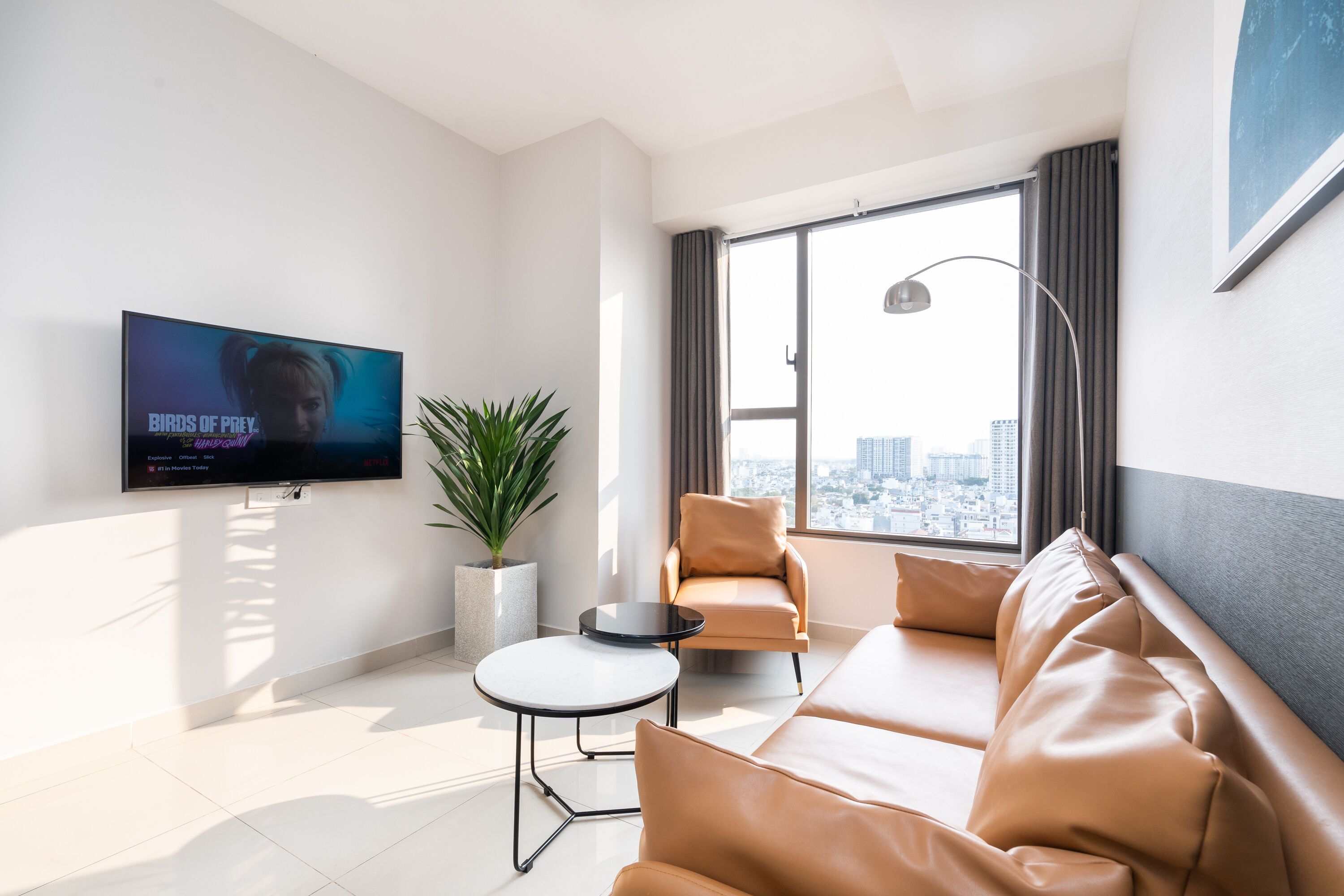 A modern living room with a large TV, a sofa, a chair, a small table, and a potted plant.