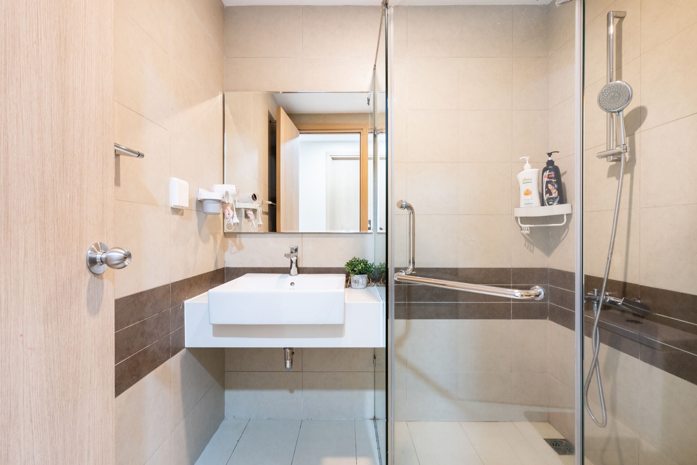 Un baño moderno con cabina de ducha de vidrio, un lavabo blanco y un estante pequeño con artículos de aseo.
