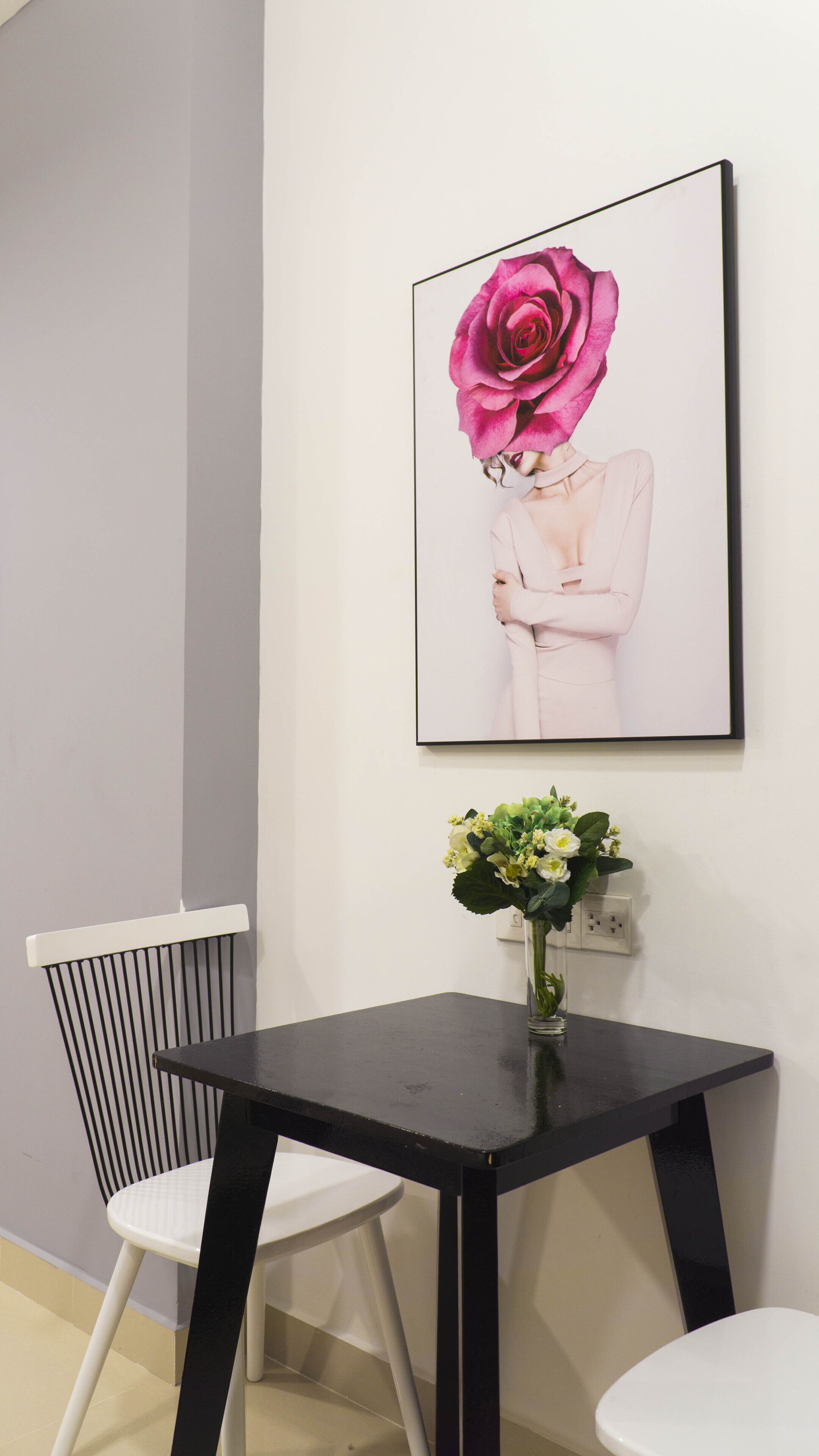 Une pièce avec une table noire, une chaise blanche et une œuvre d’art encadrée représentant une rose rose, accrochée au mur.