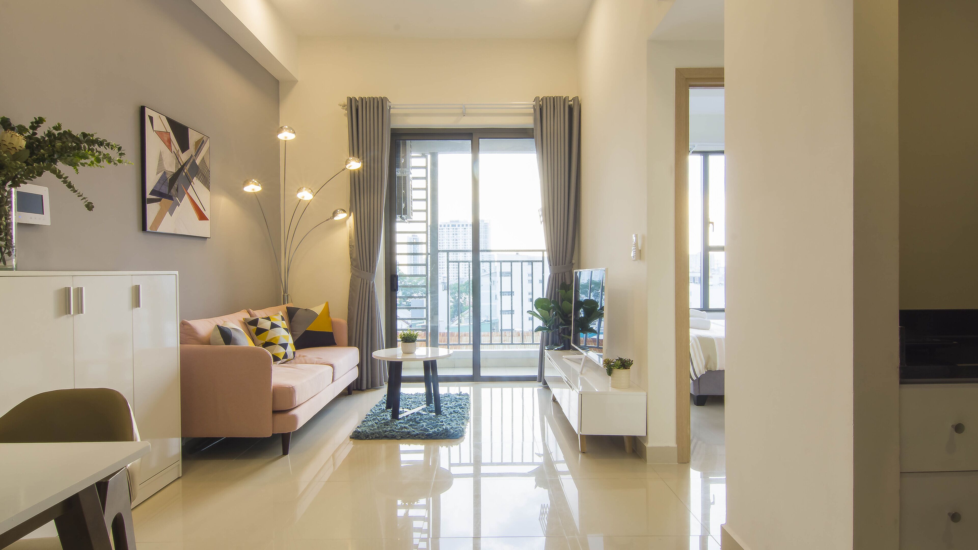 A modern living room with a sofa, a dining table, and a balcony with curtains.