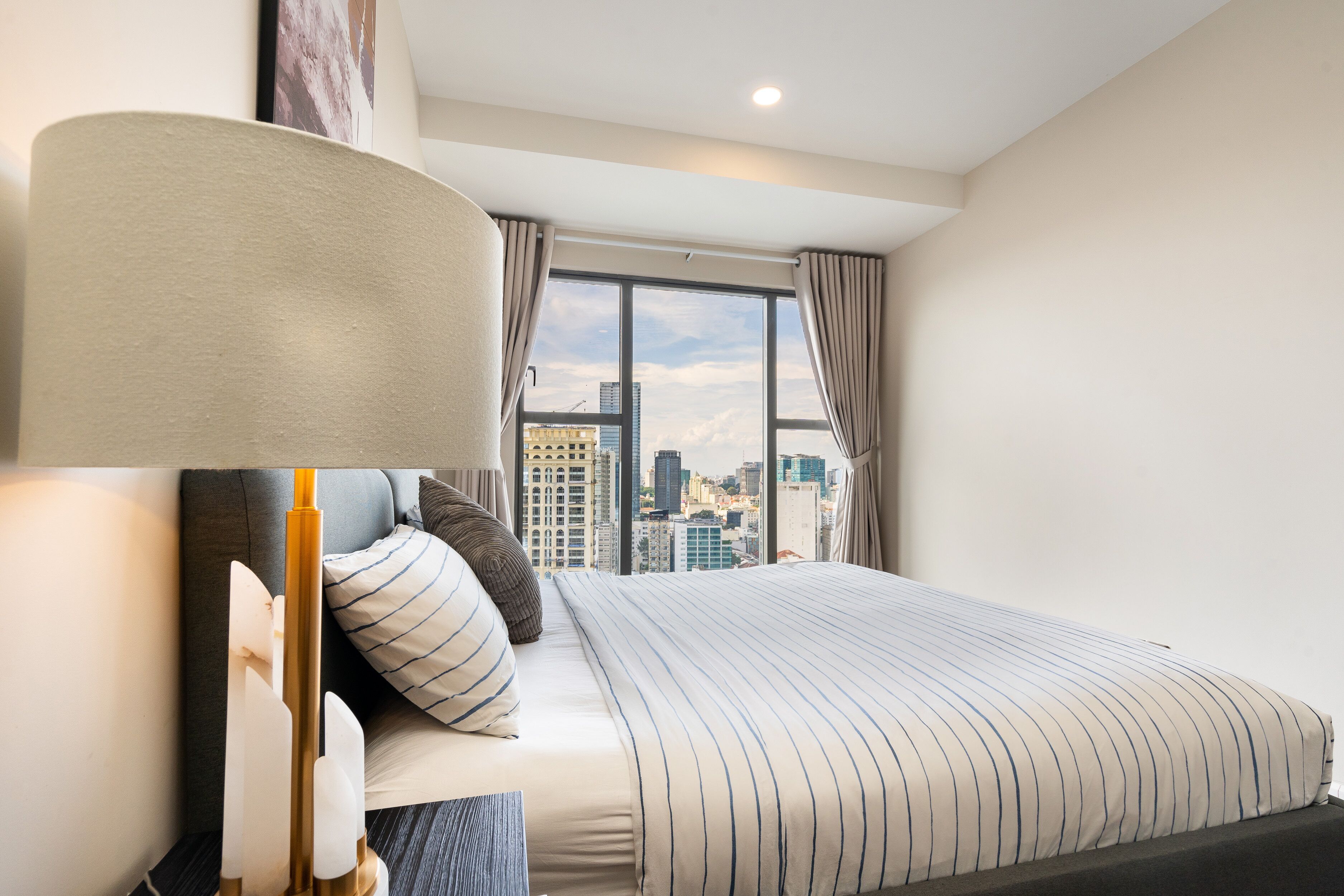 Una habitación de hotel moderna con una cama grande, vistas de la ciudad y un ventanal con cortinas.