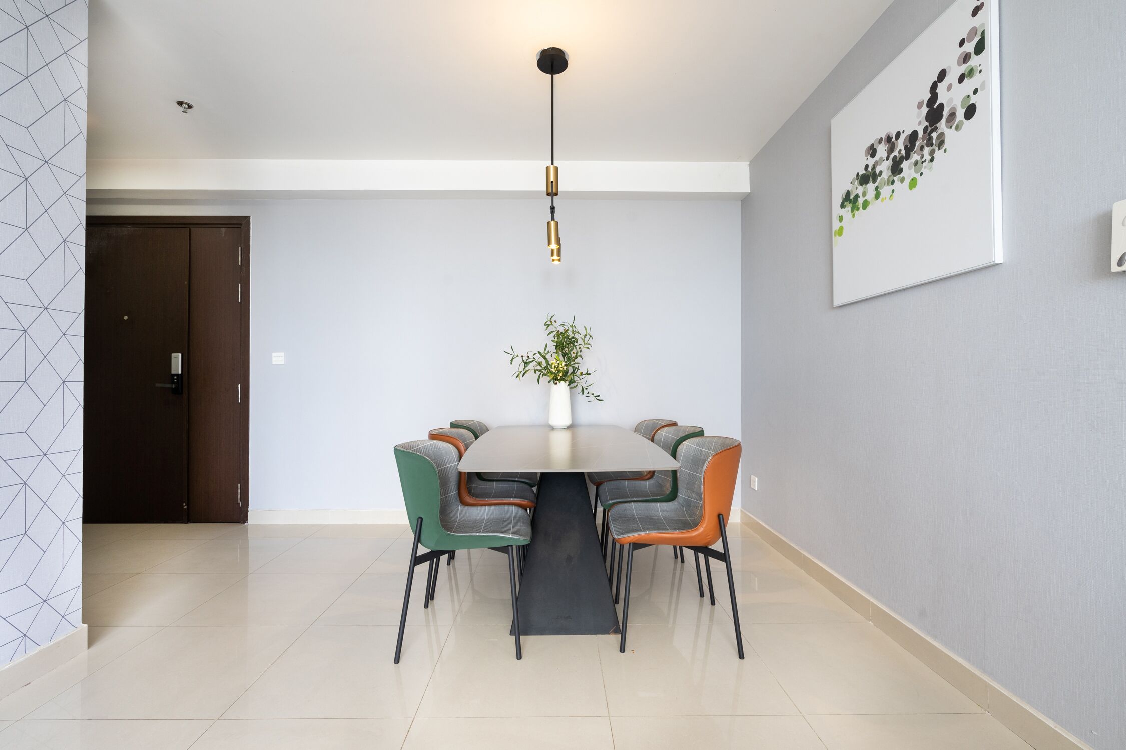 A dining area with a round table, six chairs, a vase with plants, and a ceiling light.