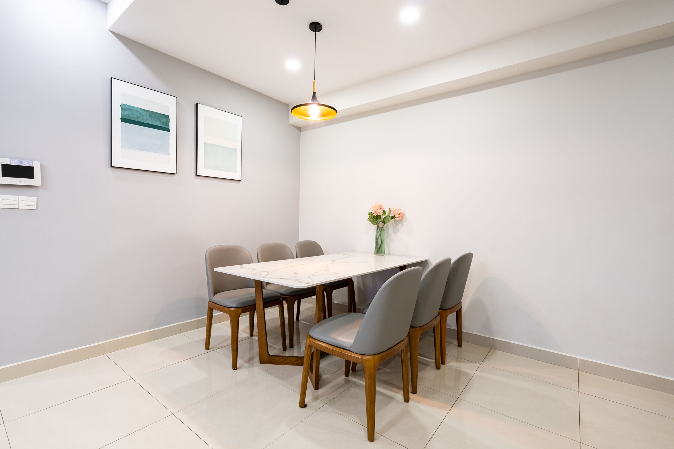 A modern dining area with a rectangular table, six chairs, a vase with flowers, and two framed artworks on the wall.