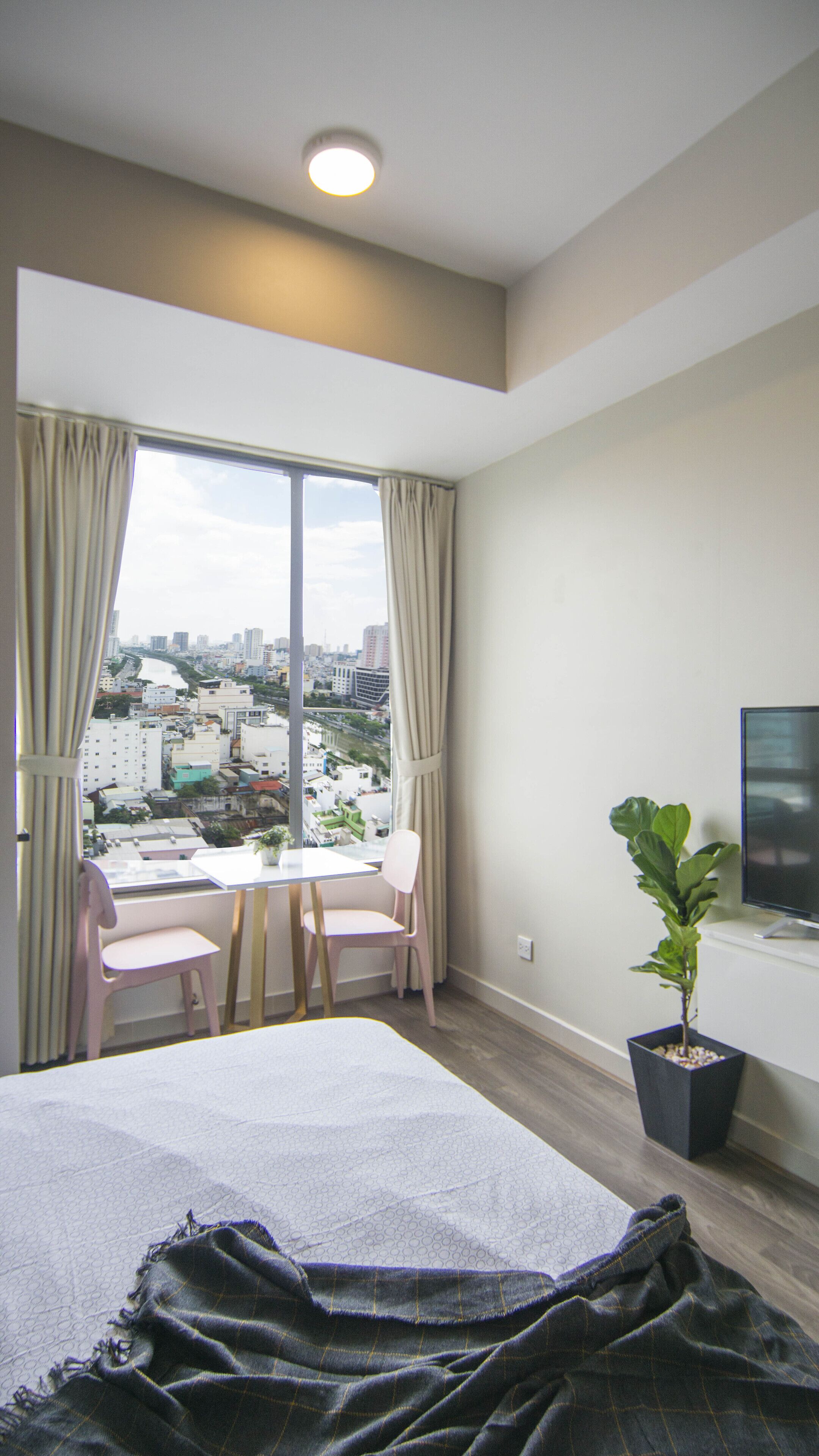 A hotel room with a bed, a desk with two chairs, a potted plant, and a TV.