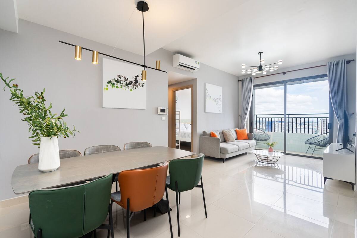 A modern living room with a dining area, a sofa set, and a balcony with a view.