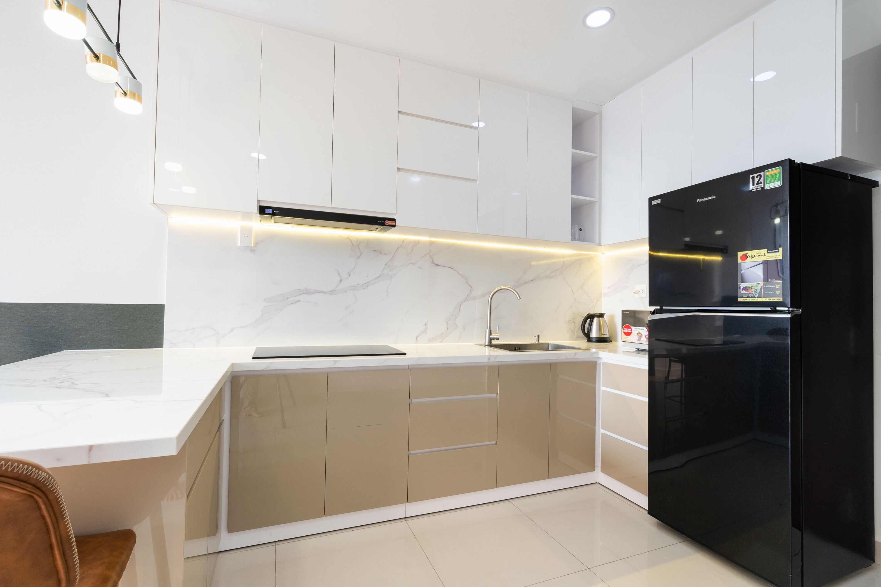 A modern kitchen with white marble countertops, beige cabinetry, and a black refrigerator.