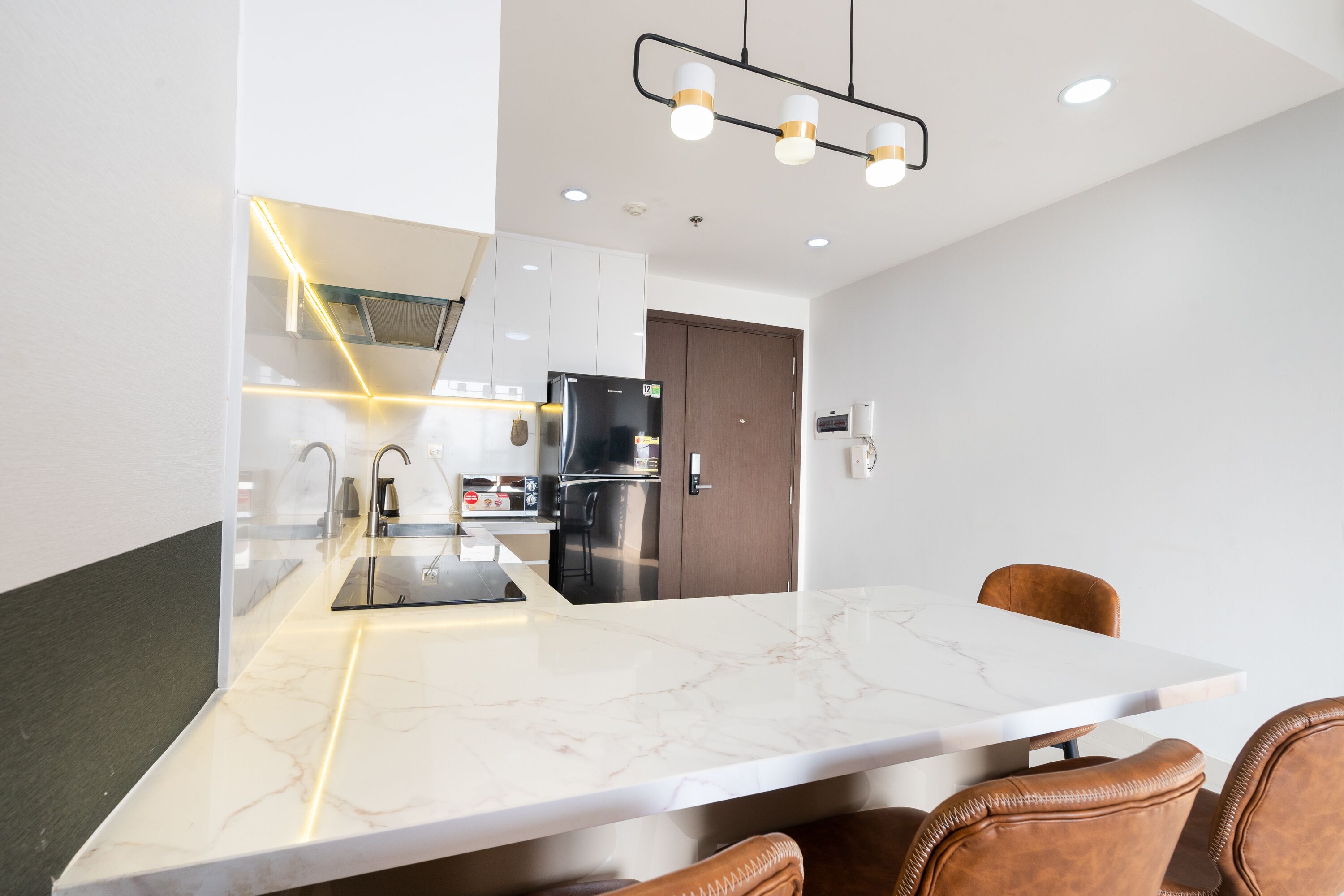 A modern kitchen with a marble countertop, stainless steel appliances, and a dining area with leather chairs.