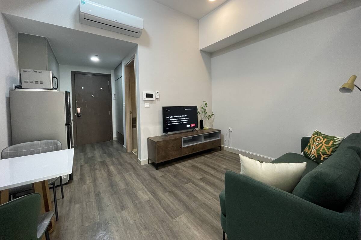 A modern living room with a flat-screen TV, a wooden entertainment unit, a green sofa, and a dining area with a white table and chairs.