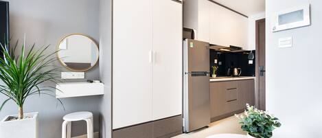 A modern kitchen with white cabinets, a stainless steel refrigerator, a round mirror, and a potted plant.
