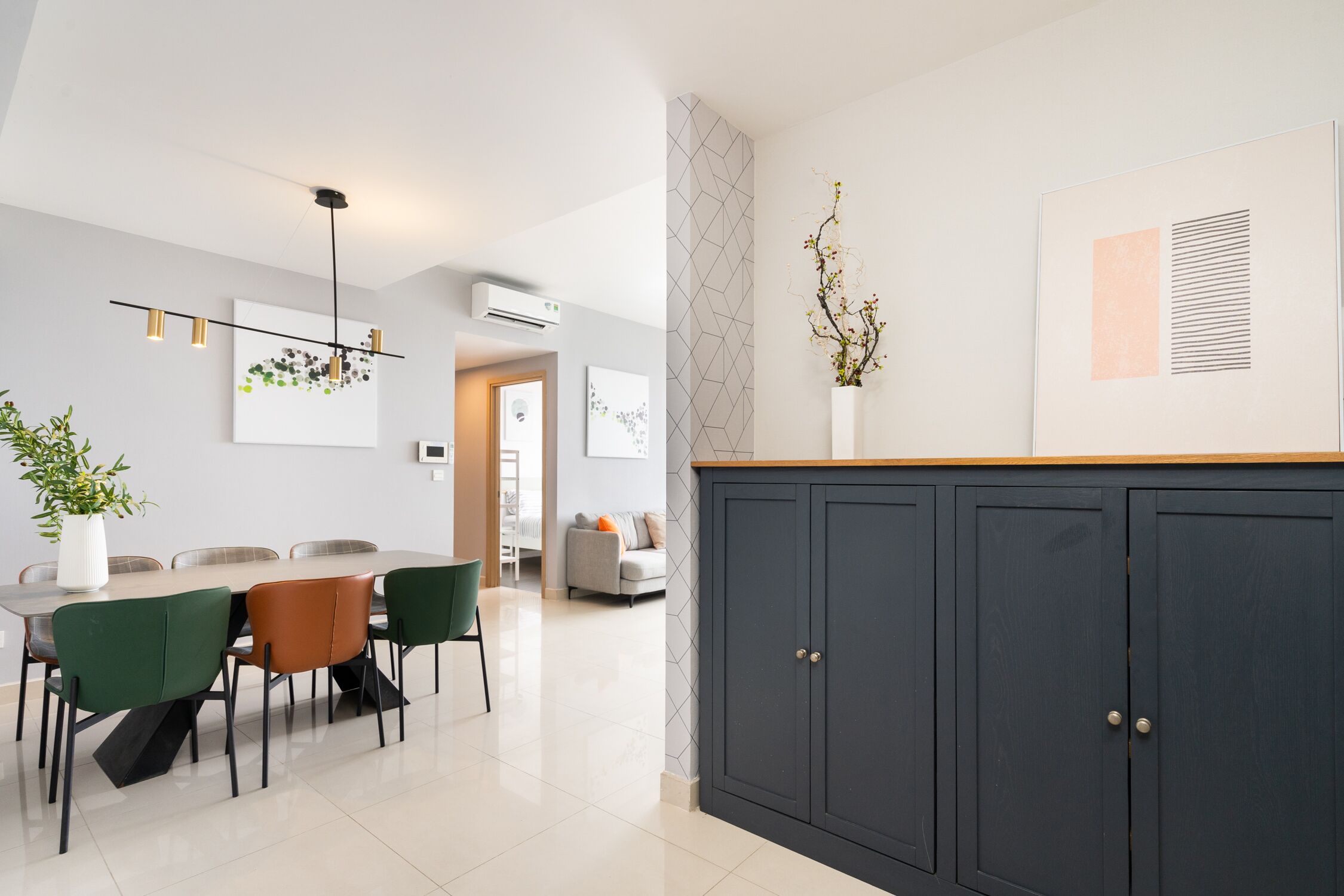 A modern dining area with a table, chairs, and a pendant light. There is a cabinet with two doors and a wall-mounted air conditioner.