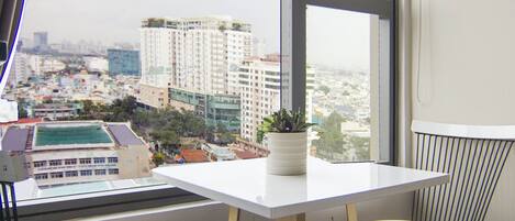 Ein kleiner Balkon mit einem weißen Tisch und zwei weißen Stühlen, mit Blick auf eine Stadtlandschaft mit Gebäuden und einem grünen Feld.