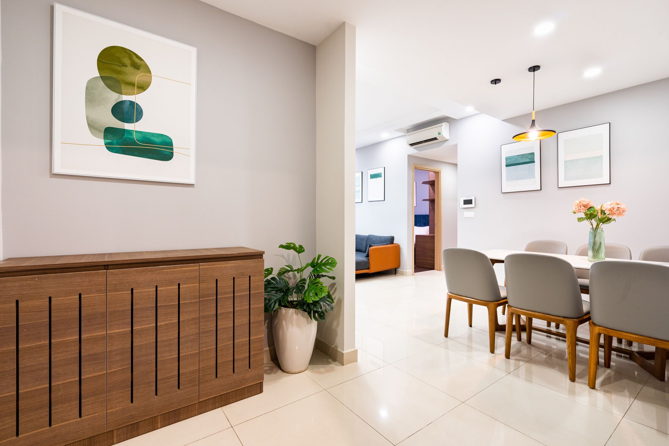A modern reception area with a wooden reception desk, a potted plant, and a dining area with a table and chairs.