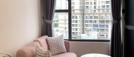A modern living room with a pink sofa, a round coffee table, and a large window with curtains.