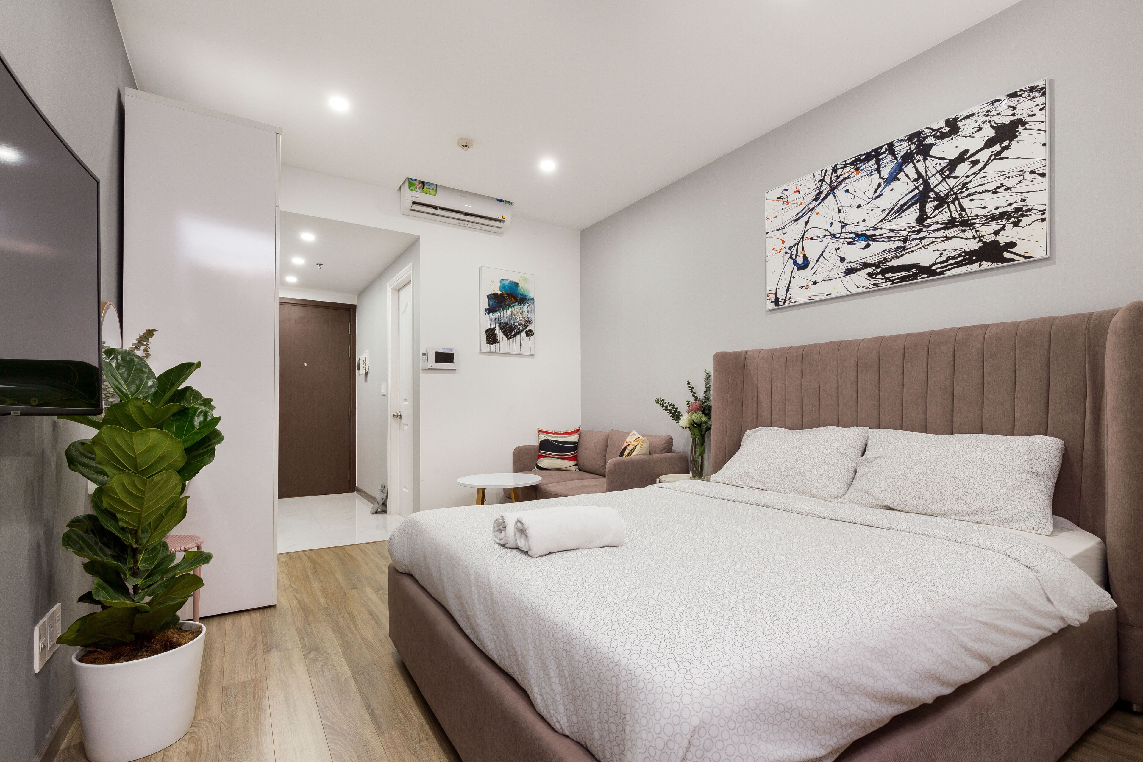 Ett modernt hotellrum med en stor säng, en krukväxt, en platt-TV och en tavla på väggen.
